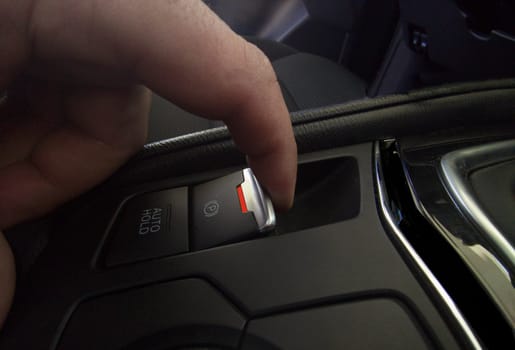 Driver pulling the electric parking brake of his car. Red color light indicating brake deactivated