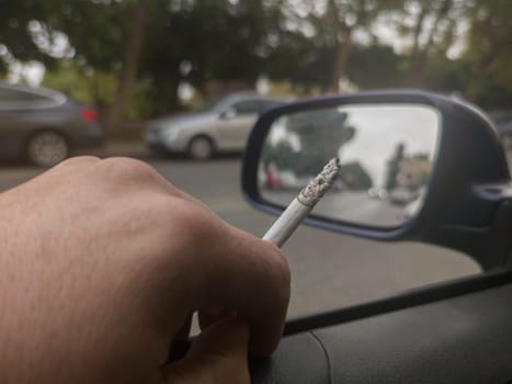 Man smoking and driving with the window down. Cause of distracted driving accidents concept