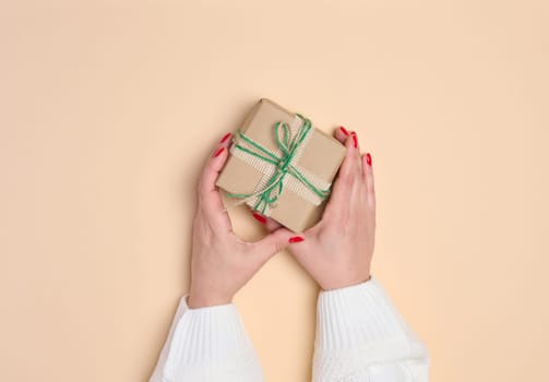 Female hands holding a gift box on a beige background. View from above