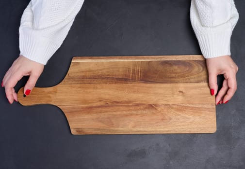 Empty wooden cutting board in female hands on black wooden table, top view