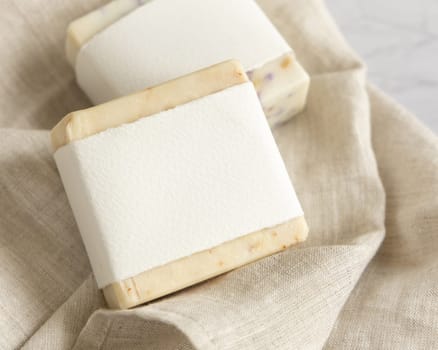 Beige handmade soap bars with blank label on linen towel close up, mockup, copy space. Natural herbal products for face and body care