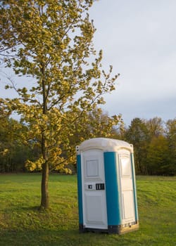 blue plastic toilet cabin in woodland at sunset