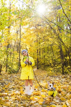 Portrait of a little girl on a background of orange and yellow leaves in an autumnal sunny day. Little puppy jack russell terrier. Pet and child concept.