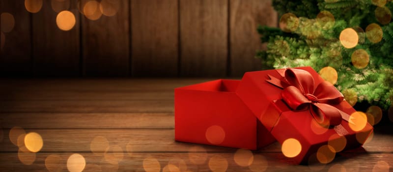 Red christmas present tied with ribbon under christmas tree with lights. Cozy magic xmas and new year holiday scene. Open gift box on rustic wooden background with copyspace.