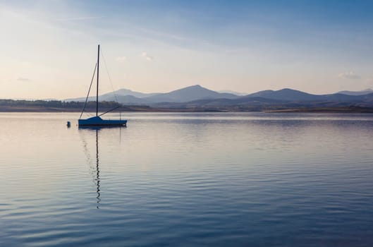 Sailing boat anchored on the shore of the Gabriel y Galan reservoir, Caceres, Spain. Active tourism at freshwaters coasts concept
