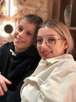 Sister and brother are sitting in a coffee shop and happily smiling.