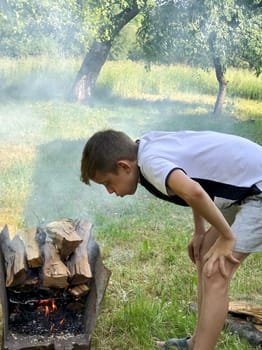 a twelve-year-old boy puts firewood in a barbecue grill in the garden