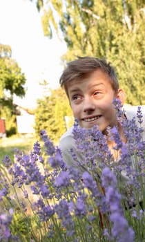 cute twelve-year-old boy in purple lavender flowers in sunlight feeling happy, having fun and showing positive and funny emotions