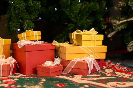Christmas gift boxes on floor under fir tree at night in living room. Winter Christmas and New year holiday concept.