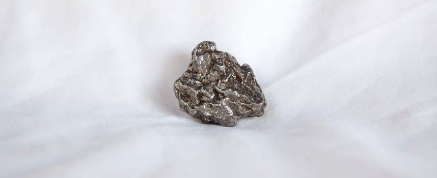 Nickel-iron type meteorite fragment. Isolated over white background. Placed over cotton cloth