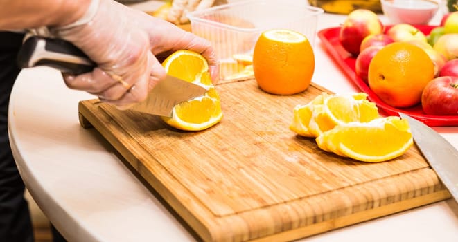 young clean chef hands cutting orange on  table.
