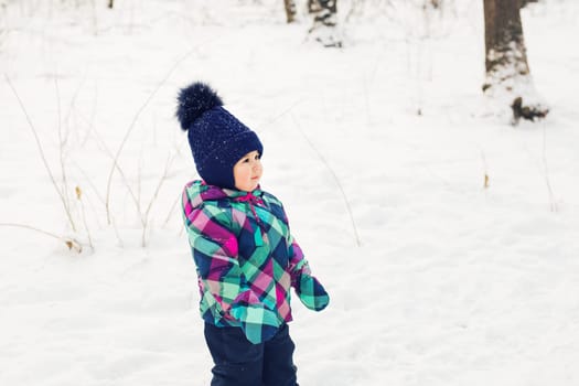 portrait of a little girl in winter clothes in snow forest at snowflakes background.