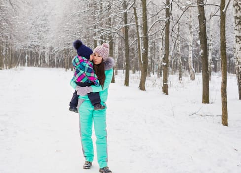 happy family mother and baby girl daughter playing and laughing in winter outdoors in the snow