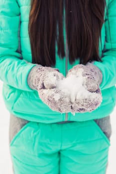 Young woman in the snow mountains landscape on holiday holding natural soft white snow in her hands to make a snowball, smiling during a cold winter day in the forest, outdoors.