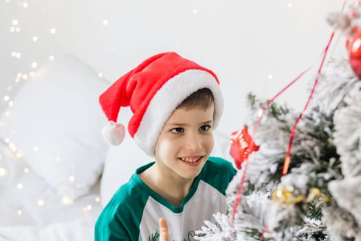 Portrait of cheerful boy smiling and laughing next to Christmas tree at house. Families and children generation alpha celebrating winter holidays.