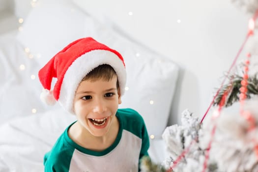 Portrait of cheerful boy smiling and laughing next to Christmas tree at house. Families and children generation alpha celebrating winter holidays.