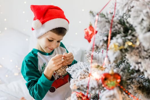 Portrait of cheerful boy smiling and laughing next to Christmas tree at house. Families and children generation alpha celebrating winter holidays.