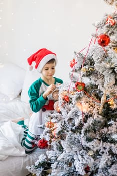 Portrait of cheerful boy smiling and laughing next to Christmas tree at house. Families and children generation alpha celebrating winter holidays.
