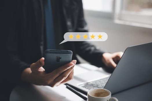 Positive feedback is a valuable business asset. A man's hand using a smartphone and laptop computer with a 5-star popup for satisfaction survey and performance evaluation