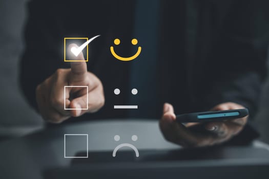Close up of a man's hand using a smartphone and laptop computer to provide positive feedback for excellent service. Concept of business satisfaction survey and digital technology