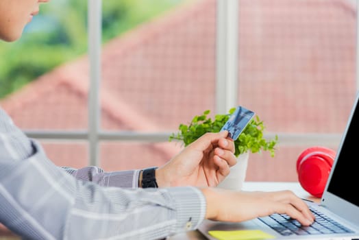 Asian business man hand holding credit card and typing entering security code on a laptop computer for process payment online shopping on the internet at the home office
