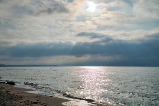 Sunset on the west beach on the Baltic Sea. Waves, beach, cloudy sky and the last rays of sunshine on the coast. Landscape photo