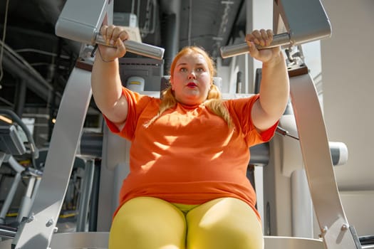 Tired sweaty obese woman breathing hard training at gym with sports equipment. Slimming and health care concept