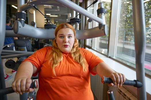 Tired sweaty obese woman breathing hard training at gym with sports equipment. Slimming and health care concept