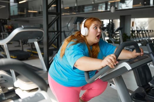 Portrait of motivated overweight woman riding exercise bike at gym. Everyday sportive routine for health and weight loss