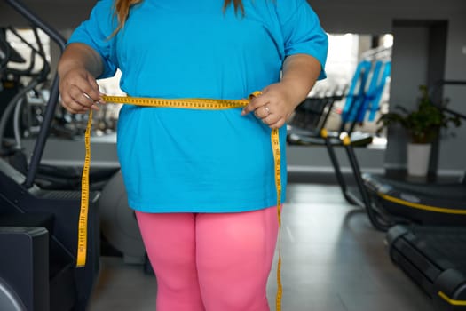 Closeup waistline of chubby woman wrapped in measuring tape. Workout sport and slimming program for people with obesity