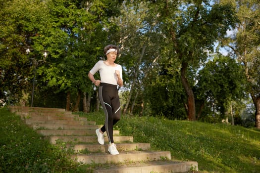 Smiling aged elderly woman jogging outdoors in city park enjoying healthy lifestyle on retirement vacation