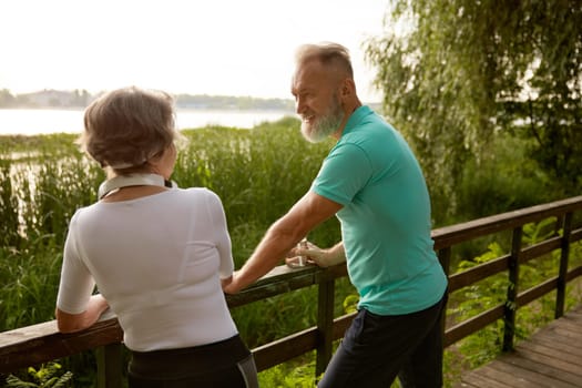 Happy elderly woman and senior man old friends having nice conversation resting after jogging workout in city park