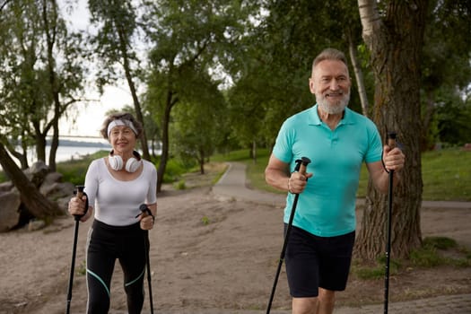 Elderly woman and man married couple enjoying nordic pole walking exercising outdoors in city park