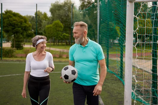 Happy retired couple doing sport at city stadium. Married man and woman seniors playing football together on weekend