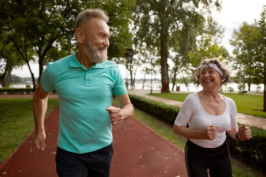 Senior couple running on track together outdoor at natural park. Happy healthy elderly woman and mature man friends exercising outdoors