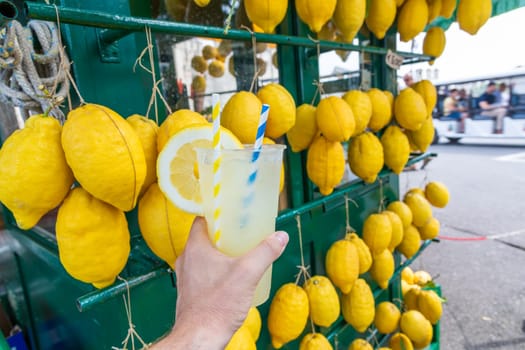 Caucasian hand with healthy fresh lemonade during summer with lemons background