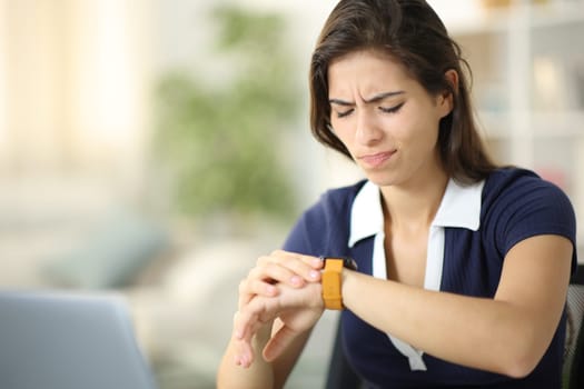 Frustrated woman checking smartwatch sitting at home