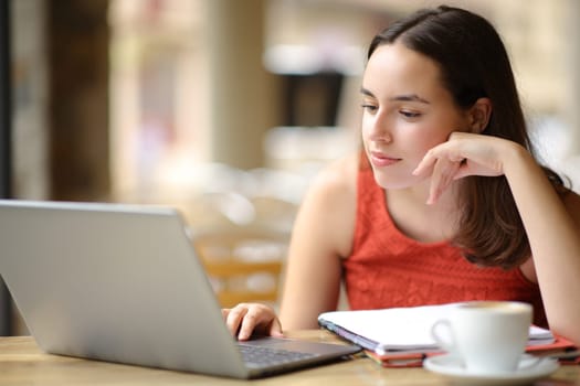 Student e-learning with laptop in a coffee shop terrace