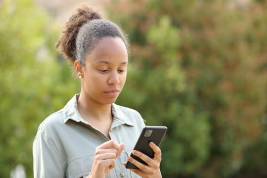 Serious black woman walking in a park checking phone