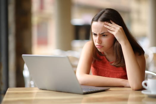 Frustrated woman checking laptop content in a bar terrace