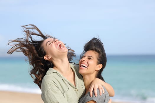 Two funny best friends laughing hilariously hugging on the beach