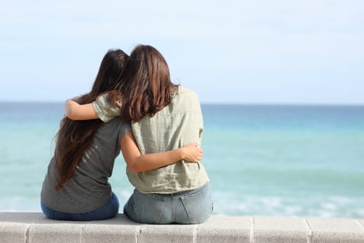 Back view portrait of two best friends hugging on the beach