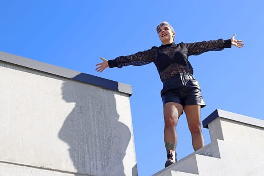 A young woman stands high up on a staircase with open arms