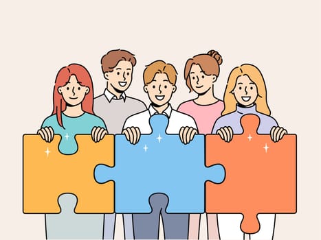 Friendly team of men and women hold giant puzzle pieces symbolizing working together to solve business problems. Business people with smile doing teamwork to increase company income