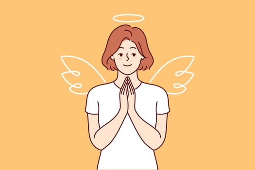 Woman with wings and angel halo stands making prayer gesture, calling on people to be kinder and more tolerant. Girl dressed as angel advertises charity fund supporting those in need.