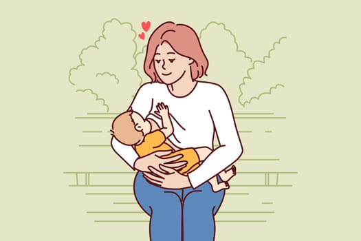 Loving mother breastfeeding baby and looks at baby lovingly sitting on park bench. Caring woman became mom calls for abandoning artificial milk nutrition and breastfeeding children.