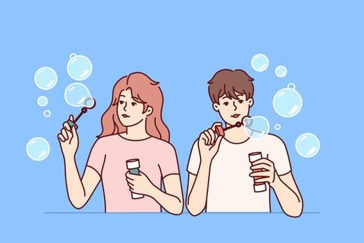 Man and woman inflate soap bubbles and have fun in free time, enjoying pastime together. Couple of casual teenagers with soap bubbles in hands playing and refusing to do useful things