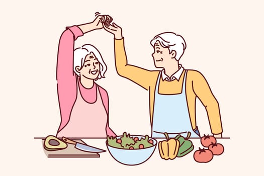 Elderly couple of vegans cooks dinner and dances together, calling for healthy lifestyle and giving up meat. Man and woman of retirement age, have become vegans feel surge of strength and energy