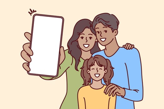 Happy family holds phone with blank screen in hands, offering to use advertising mobile application. Mom, dad and daughter are laughing demonstrating phone with place for ads website