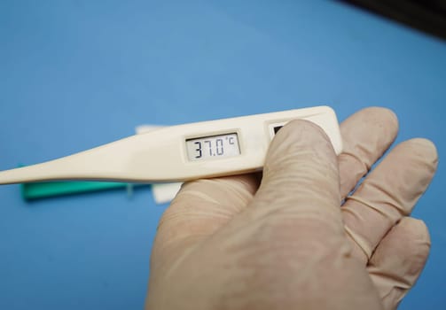 Hand with digital clinical thermometer and syringe on blue background